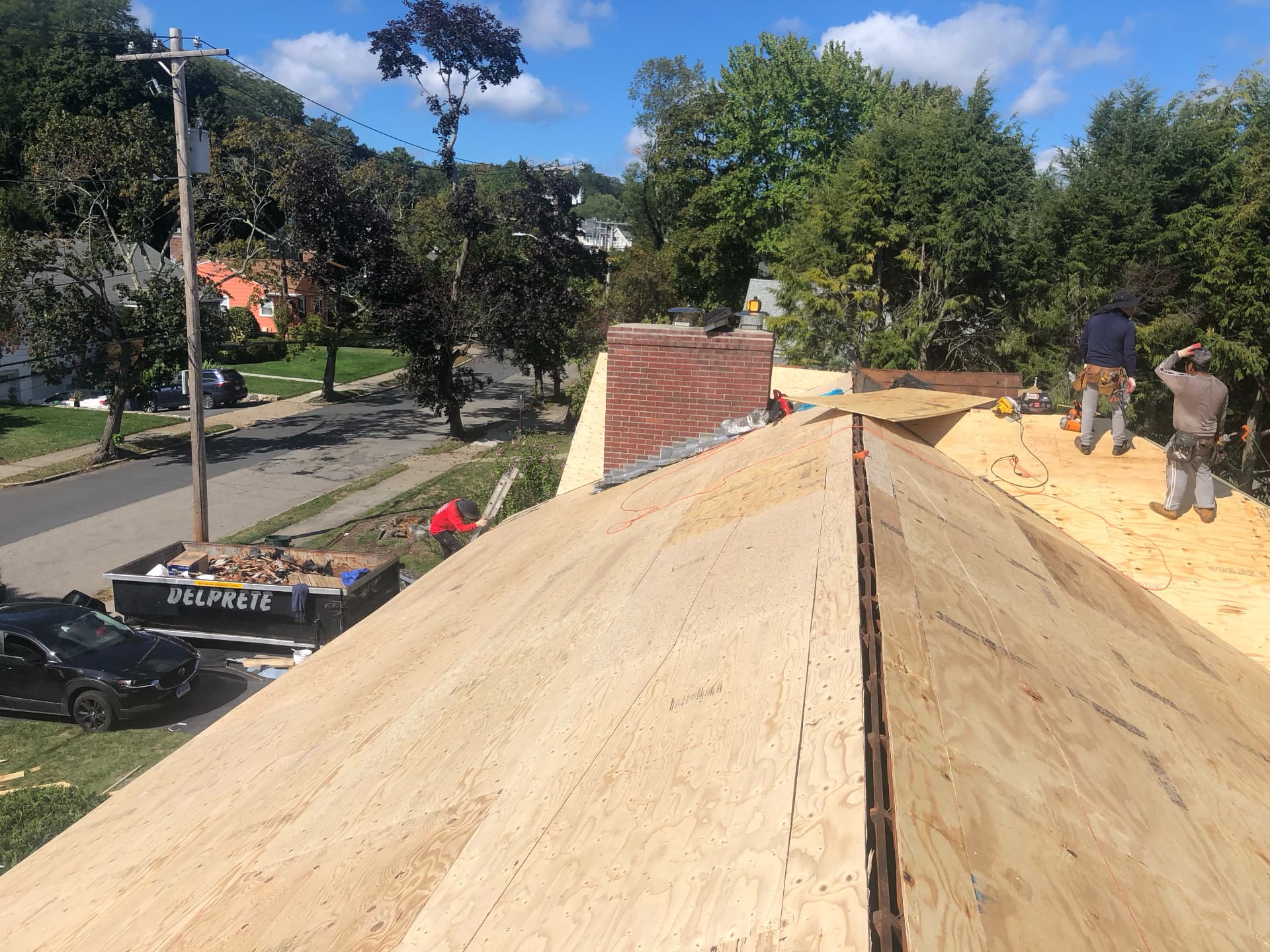 Crew installing new plywood roof decking next to a brick chimney