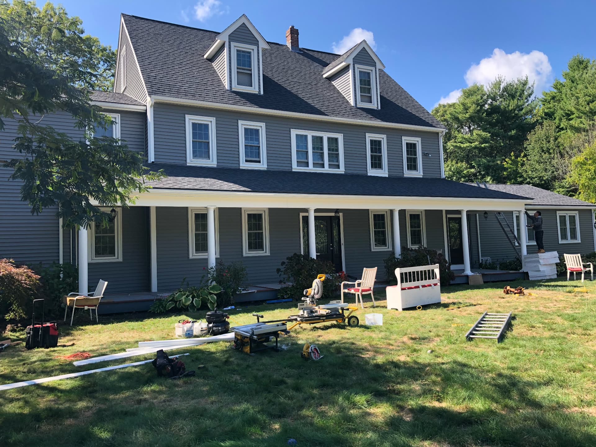 Large colonial home with new gray vinyl siding, white trim, and a wraparound porch