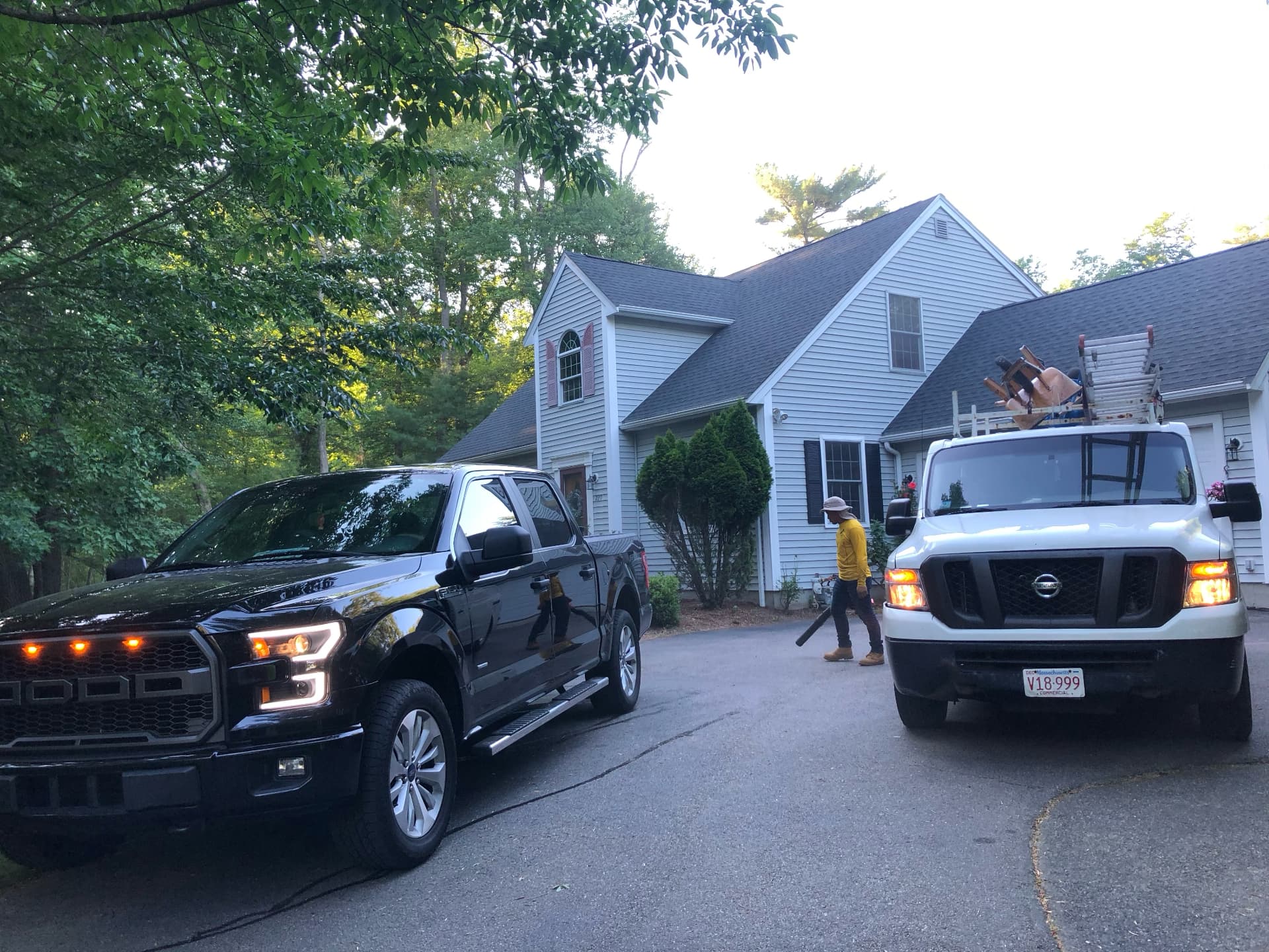 Finished shingle roof on a gray colonial home with KCG work trucks in the driveway