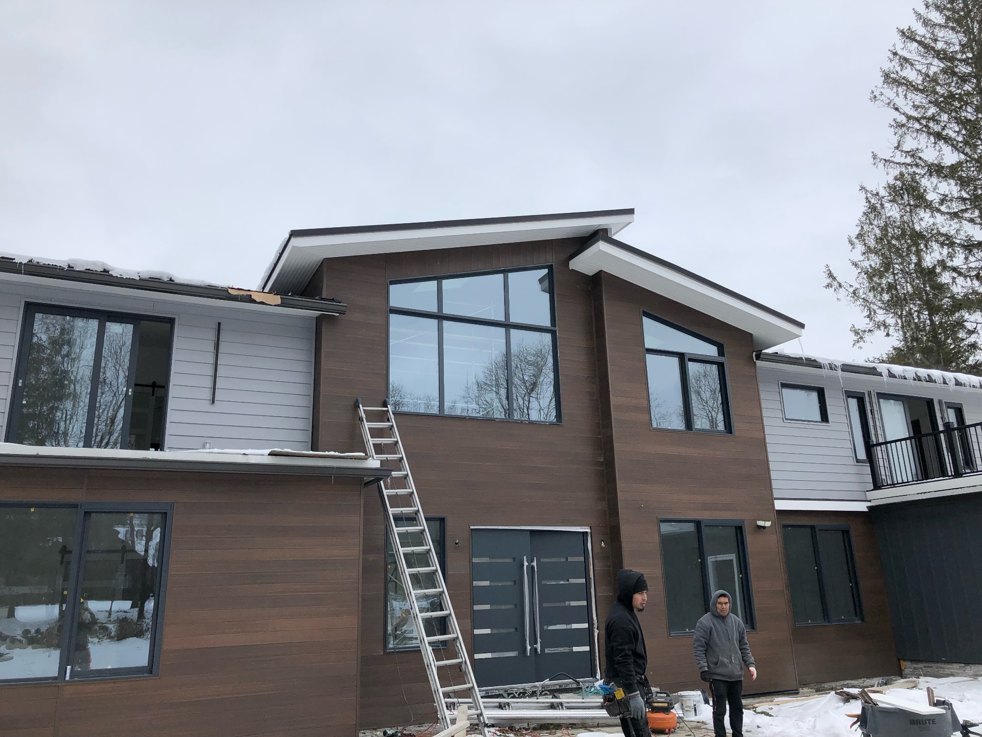 Modern home with new wood-look and gray lap siding, large black windows, and crew on site